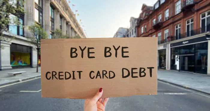 Person holding a cardboard sign that reads Bye Bye Credit Card Debt